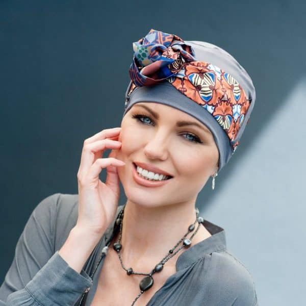 Woman with hair loss wearing grey bamboo hat with delicate patterned scarf tied around the hat.