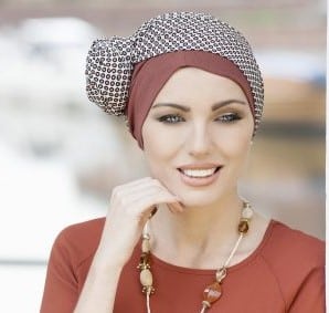 Woman with no hair wearing a soft brown Brick Polka Dot Hat with a patterned scarf.